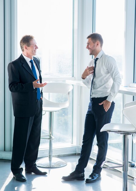 Two smiling businessmen standing near window having conversation in office