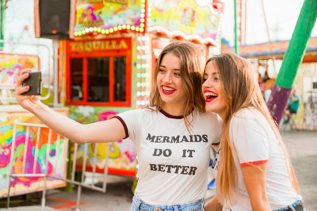 Two smiling female friends taking selfie on cellphone