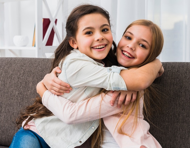 Free photo two smiling girl embracing each other looking to camera at home