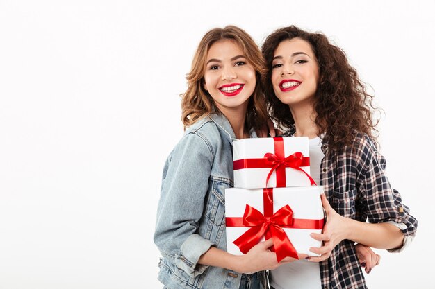Two smiling girls posing with gifts  over white wall