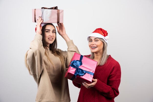 お祝いのクリスマスプレゼントを保持しているサンタの帽子の2人の笑顔の女の子。