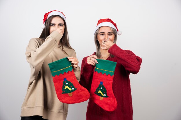 크리스마스 양말을 신고 산타 모자를 쓴 두 명의 웃는 소녀가 혐오감으로 코를 닫습니다.