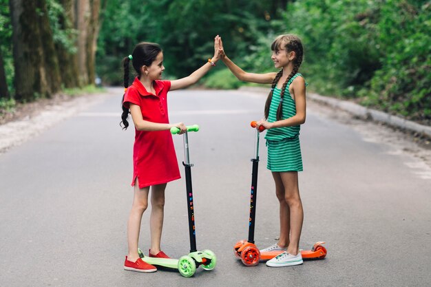 Two smiling girls standing on scooter giving high five gesture on road