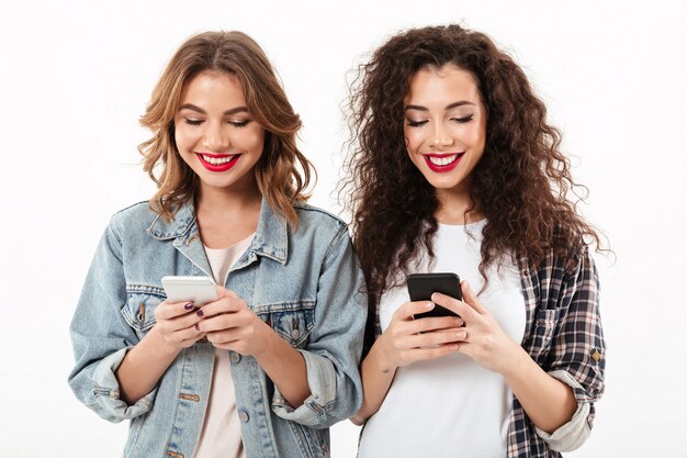 白い壁にスマートフォンでメッセージを書く2つの笑顔の女の子