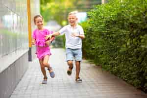 Бесплатное фото Два улыбающихся ребенка, мальчик и девочка вместе бегают по городу, городу в летний день
