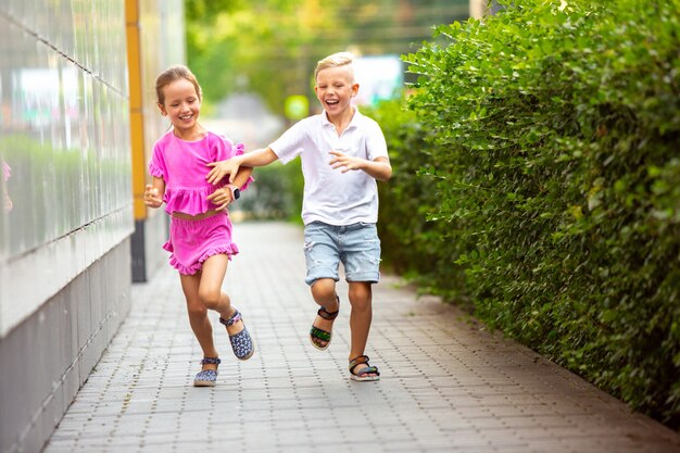 Two smiling kids, boy and girl running together in town, city in summer day