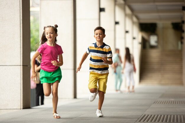 Два улыбающихся ребенка, мальчик и девочка вместе бегают по городу, городу в летний день