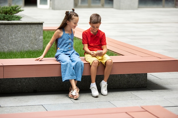 Two smiling kids, boy and girl running together in town, city in summer day