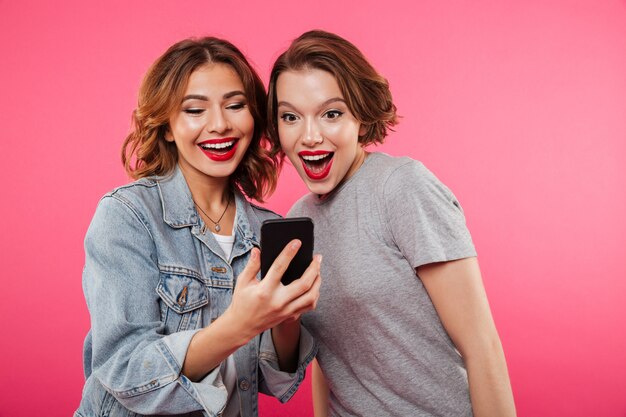 Two smiling ladies friends using mobile phone.