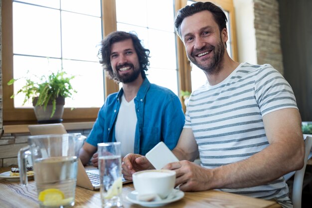 コーヒーショップでテーブルに座って二笑顔の男性