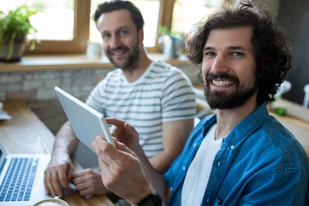 Two smiling men using digital tablet at coffee shop