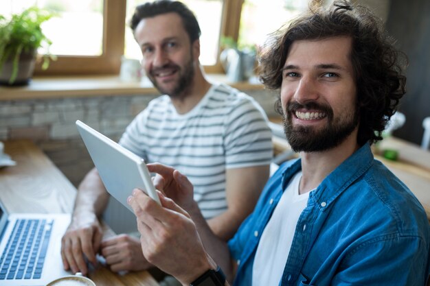 Two smiling men using digital tablet at coffee shop