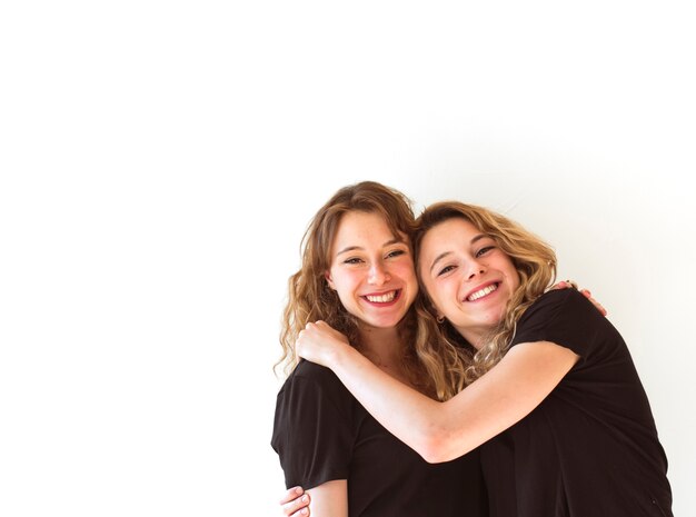 Two smiling sisters embracing on white background