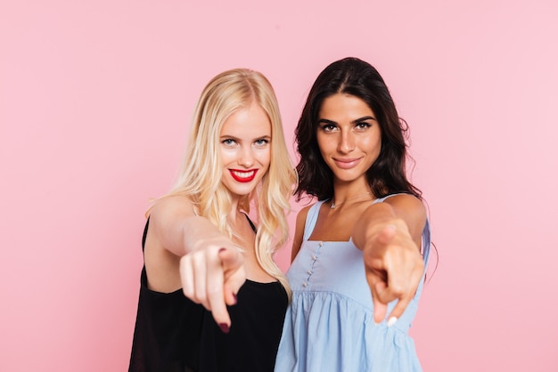 Free photo two smiling women pointing and looking at the camera