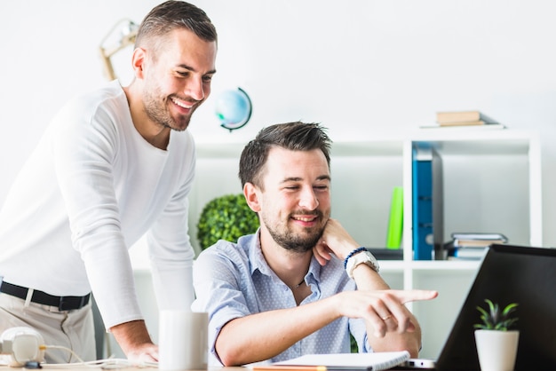 Two smiling young businessmen looking at laptop screen