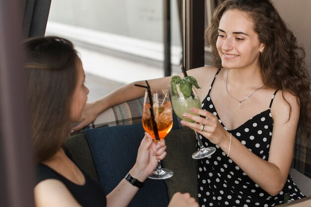 Two smiling young female friends toasting cocktail glasses