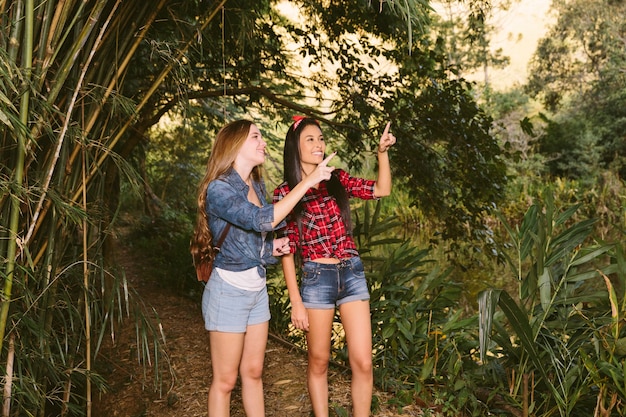 Two smiling young women pointing upwards in forest