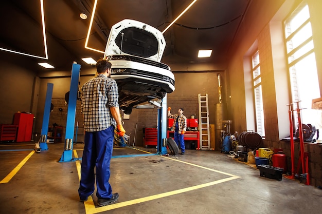 Two specialists in uniform repairing car together in garage