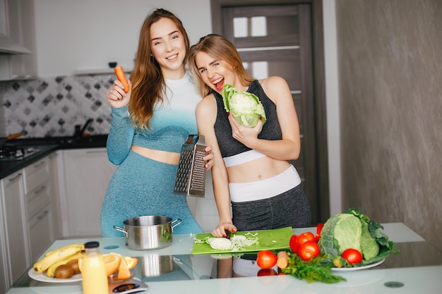 Two sports girl in a kitchen with vegetables