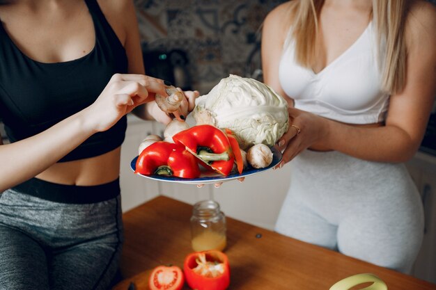 Two sports girl in a kitchen with vegetables