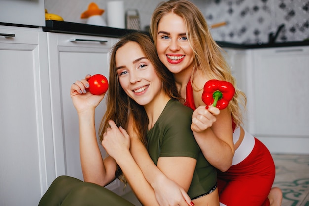 Two sports girls in a kitchen with vegetables