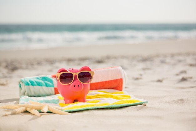 Two starfish and piggy bank with sunglasses on beach blanket