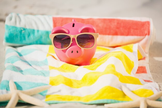 Two starfish and piggy bank with sunglasses on sand