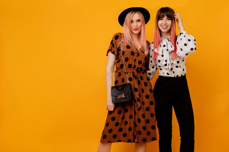 Free Photo two stylish elegant women in dresses posing over yellow wall
