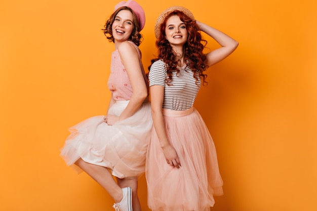 Due ragazze alla moda che ballano con il sorriso. studio shot di adorabili signore alla moda isolato su sfondo giallo.