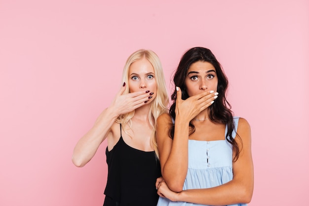 Two surprised women covering her mouths and looking at camera