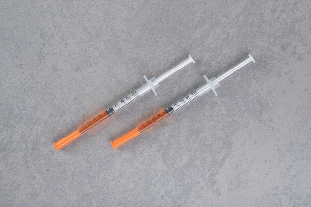 Two syringes with brown liquid on gray surface