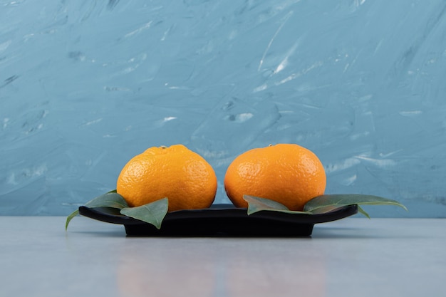 Two tasty clementine fruits on black plate