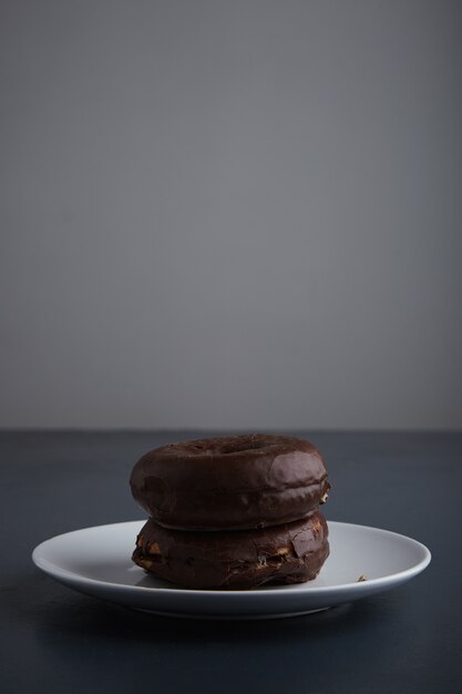 Two tasty freshly baked donuts glazed with chocolate on white ceramic small plate isolated  on rustic old blue wooden table. side view