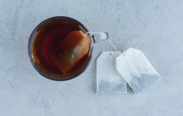 Two tea bags next to a glass of tea on marble.