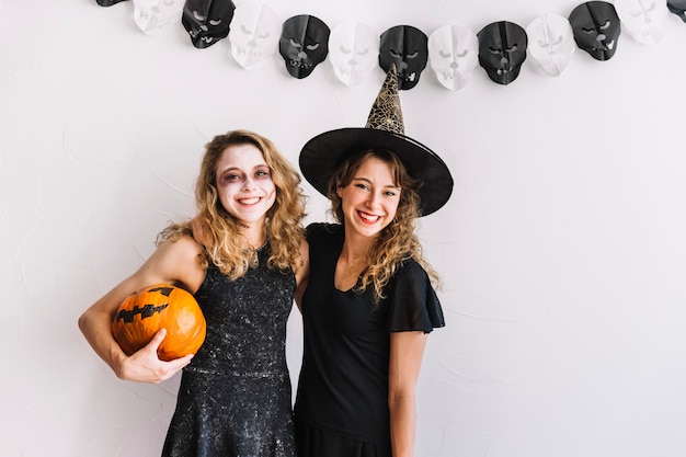 Two teenage girls in Halloween suits hugging holding pumpkin