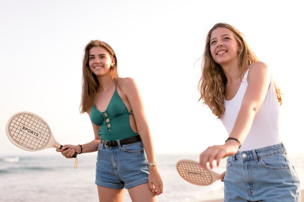 Two teenage girls playing tennis with racket at beach