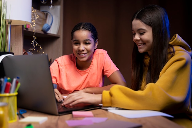 Two teenage girls studying together at home on laptop
