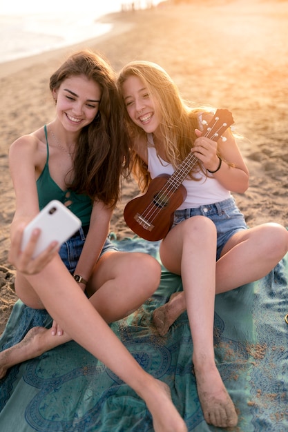 Two teenage girls taking selfie at beach during sunny day