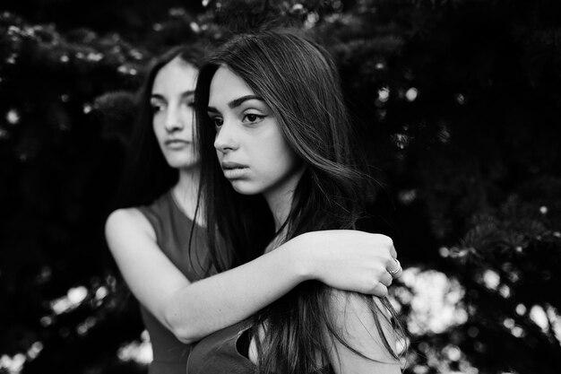 Two teenagers girl in blue and red dresses posed outdoor and hugging