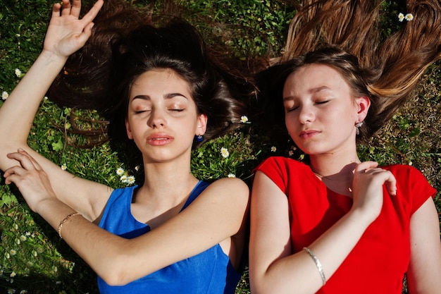 Free photo two teenagers girl in blue and red dresses posed outdoor and lying on grass