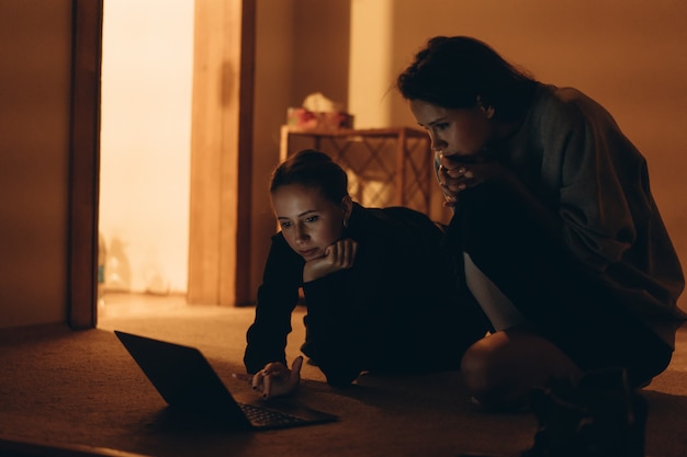 Two teens watching on line content in a laptop lying on the floor
