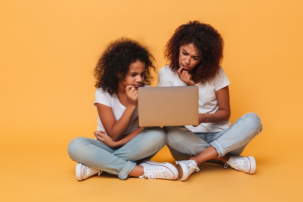 Two thoughtful afro american sisters using laptop computer