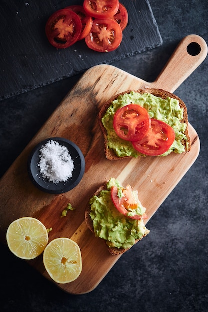 two toast with avocado and tomatoes with salt and lemon on a chopping board