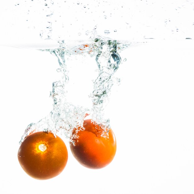 白い背景の上に水に落ちる2つのトマト