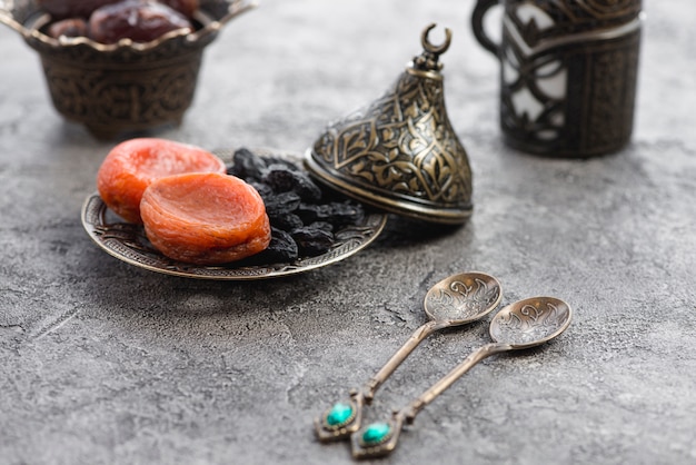 Two traditional metallic spoons in front of dried apricot and black raisin on plate