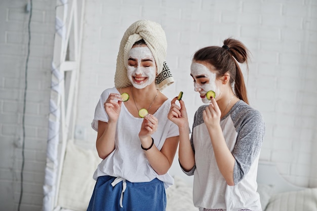 Free photo two twins girls in pajamas with facial mask and cucumber slices