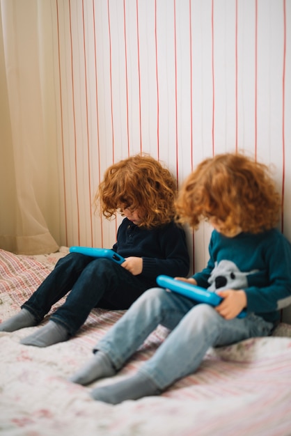 Foto gratuita sorella dei due gemelli che si siede sul letto che esamina le compresse digitali portatili