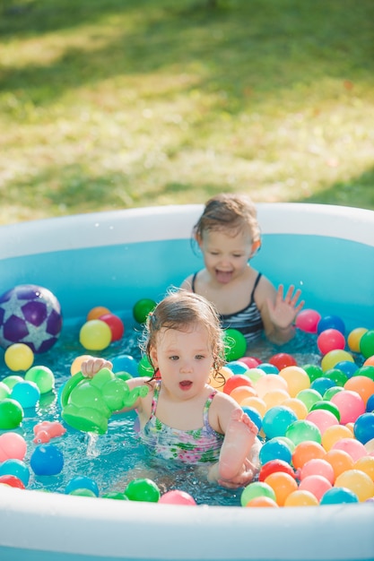 夏の晴れた日に膨脹可能なプールでおもちゃで遊ぶ2歳の小さな女の赤ちゃん