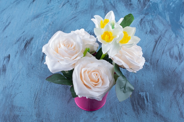 Two types of flowers placed in pink bucket on blue.