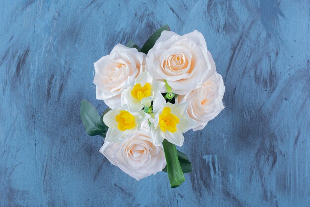 Two types of flowers placed in pink bucket on blue.